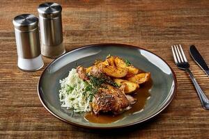 Grilled chicken leg with chips potatoes and cabbage on plate on a wooden table. photo