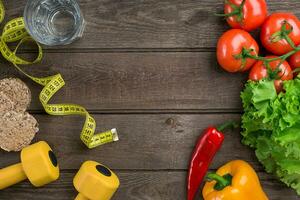 Sport and diet. Vegetables, dumbbells and centimeter. Peppers, tomatoes, salad on rustic background photo