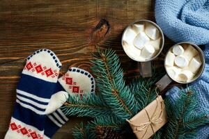 Two cups of hot cocoa or chocolate with marshmallow, mittens, christmas decor and fir tree on wooden rustic background from above. photo
