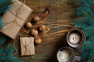 Navidad regalos con dos tazas de capuchino, nueces, conos y abeto rama en de madera antecedentes cerca arriba foto