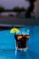 Rum cola casual cocktail with ice cubes and lime at summer bar stand background. photo