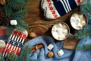 Two cups of hot cocoa or chocolate with marshmallow, mittens, christmas decor and fir tree on wooden rustic background from above. photo