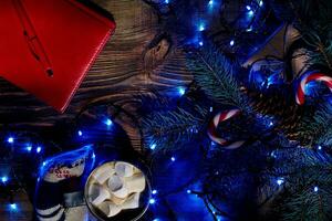 Christmas hot drink. Cocoa with marshmallow, garland and spruce branches on a wooden background. Top view photo