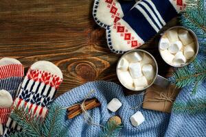 Two cups of hot cocoa or chocolate with marshmallow, mittens, christmas decor and fir tree on wooden rustic background from above. photo