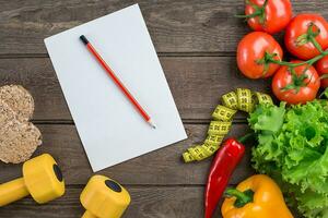 Sport and diet. Vegetables, dumbbells and centimeter. Peppers, tomatoes, salad on rustic background photo