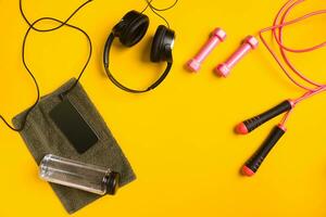 Fitness accessories on yellow background. Towel, bottle of water, headphones and smart. photo