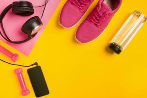 Fitness accessories on yellow background. Sneakers, bottle of water, headphones and smart. photo