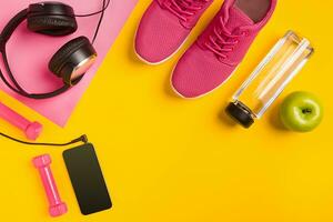 Fitness accessories on yellow background. Sneakers, bottle of water, headphones and smart. photo