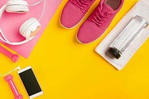 Fitness accessories on a yellow background. Sneakers, bottle of water, earphones and dumbbells. photo