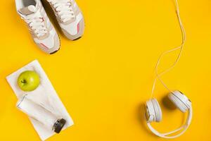 Athlete's set with female clothing, headphones and bottle of water on yellow background photo