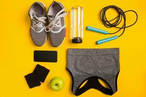 Fitness accessories on a yellow background. Sneakers, bottle of water, apple and sport top. photo