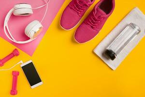 Fitness accessories on a yellow background. Sneakers, bottle of water, earphones and dumbbells. photo