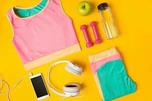 Sport equipment and clothes with mobile phone on yellow background. Top view photo