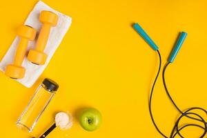 Athlete's set with female clothing, dumbbells and bottle of water on yellow background photo