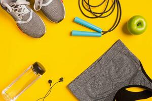 Fitness accessories on yellow background. Sneakers, bottle of water, headphones and sport top. photo