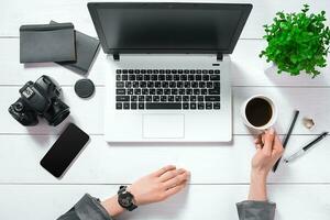 Flat lay, top view office table desk. Workspace with girl's hands, laptop, green flower in a pot, black diary, coffee mug photo