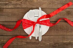 valentine's day background, white plate, fork, knife, tape hearts on old wooden table, photo