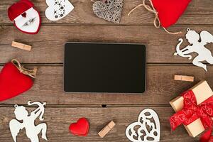 Valentines day hearts, ring, gift box and the tablet over wooden background. photo