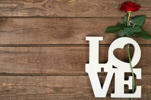 Red rose and ring over wooden background photo