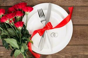 parte superior ver de cerca de romántico cena servicio con un ramo de flores rojo rosas y anillo encima el blanco plato foto
