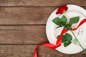 Top view closeup of romantic dinner serving with a red rose and ring above the white plate photo