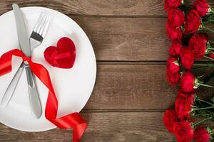 san valentin día mesa ajuste con lámina, tenedor, cuchillo, rojo corazón, cinta y rosas. antecedentes foto