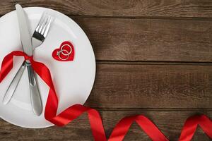 Valentines day table setting with plate, fork, knife, red heart, ring and ribbon. background photo