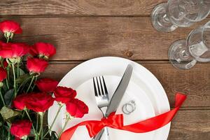 parte superior ver de cerca de romántico cena servicio con un ramo de flores rojo rosas y anillo encima el blanco plato foto