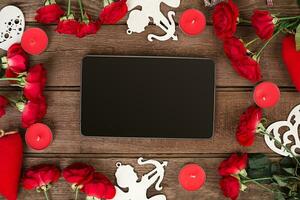 Frame of rose flowers with the tablet on wooden background photo