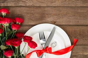 Valentine's Day dinner table setting with red ribbon, roses, knife and fork ring over oak background. photo