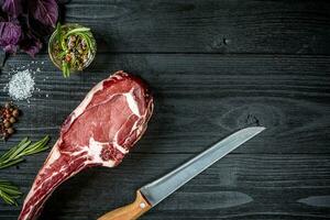 Fresh raw beef with basil and a sprig of rosemary with knife with a wooden handle on black wooden background. Top view photo