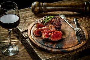 Grilled ribeye beef steak with red wine, herbs and spices on wooden table photo