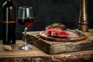Grilled ribeye beef steak with red wine, herbs and spices on wooden table photo