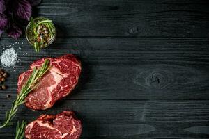 Fresh raw beef with basil and a sprig of rosemary on black wooden background photo