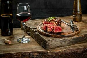 Grilled ribeye beef steak with red wine, herbs and spices on wooden table photo