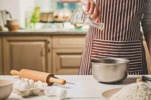 Young woman pouring oil into a bowl with dough, close-up photo