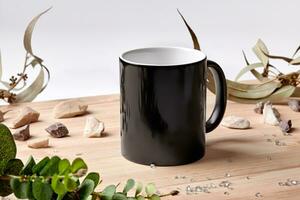 Black ceramic mug on wooden desktop next to scattered crystals, green twigs and small stones against white background. Close up, copy space photo