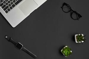 Metallic notebook or laptop, glasses, smartwatch and two green succulents in white pots on black studio background. Close up, copy space photo