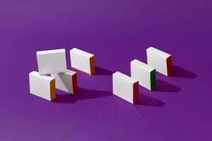 Seven small shadow-casting cardboard boxes or packs with colorful sides and no logo on purple studio background. Close up, copy space photo