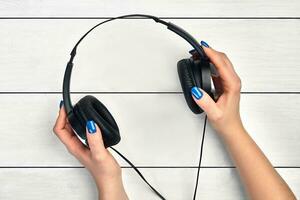 Hands of a woman are holding black headphones against white wooden background. Concept of modern technologies. Close up, copy space photo