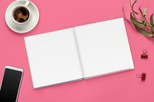 Smartphone with black screen, empty open notepad, two binder clips, cup of coffee and green twig on pink studio background. Close up, copy space photo