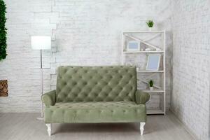 Living room interior with gray sofa against white brick wall. Modern lamp, shelving with empty photo frames and green plants in pots. Copy space