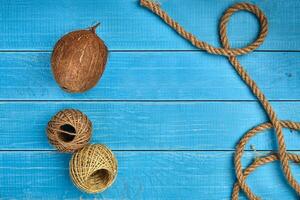 Ripe coconut, two skeins of jute twine or thread and a rope on blue wooden background or desktop. Close up, copy space photo