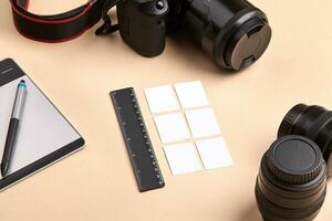 Camera with lenses, graphics drawing tablet and stylus pen, black ruler and six small sheets of paper over pink background. Close up, copy space photo