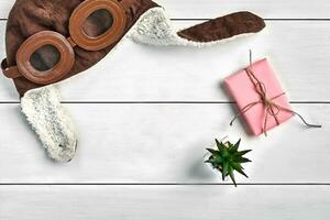 Warm brown hat, pink gift box tied by jute thread and green succulent in a pot on white wooden background. Close up, copy space photo