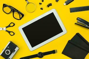 Flat lay display of business office gadgets with notepad, vintage camera, pen, develop, glasses and etc. Top view. Black office objects on a yellow background photo