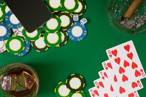 gambling, fortune and entertainment concept - close up of casino chips, whisky glass, playing cards and cigar on green table surface photo