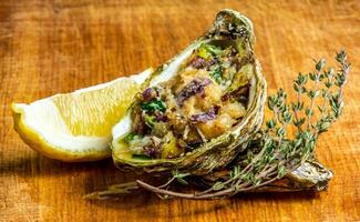 Baked oyster shell with cheese, served greens and lemon photo