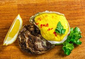 Baked oyster shell with cheese, served greens and lemon photo