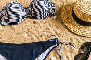 Summer bikini and accessories stylish beach set, Beach bikini summer outfit and sea sand as background, Top View, Concept photo